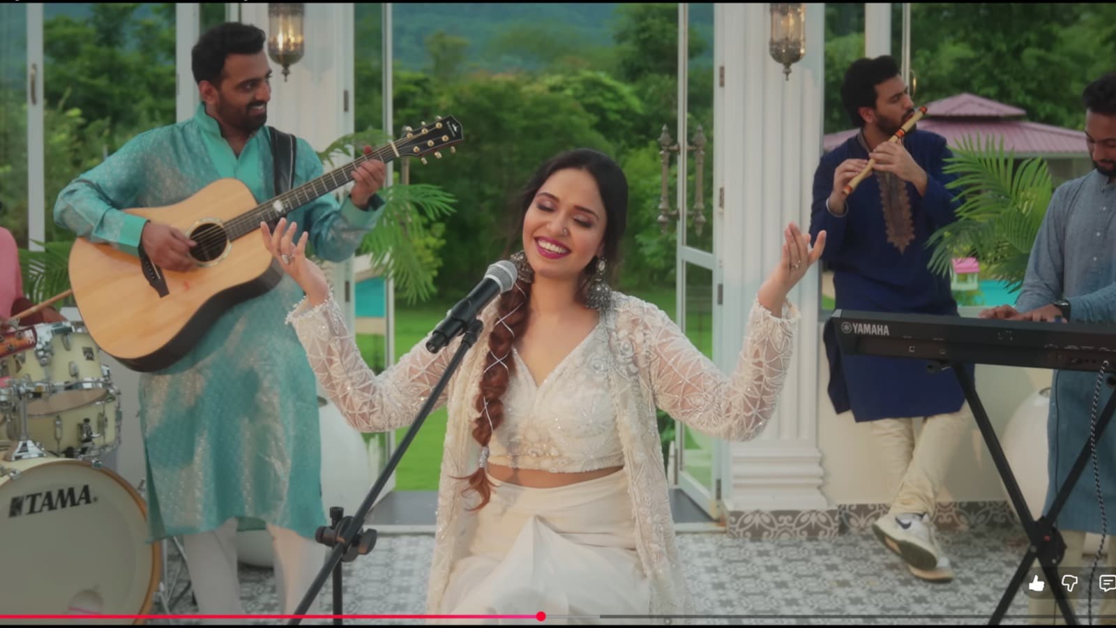 Aishwarya Anand on stage in a flowing indigo outfit, hand raised in rendition
